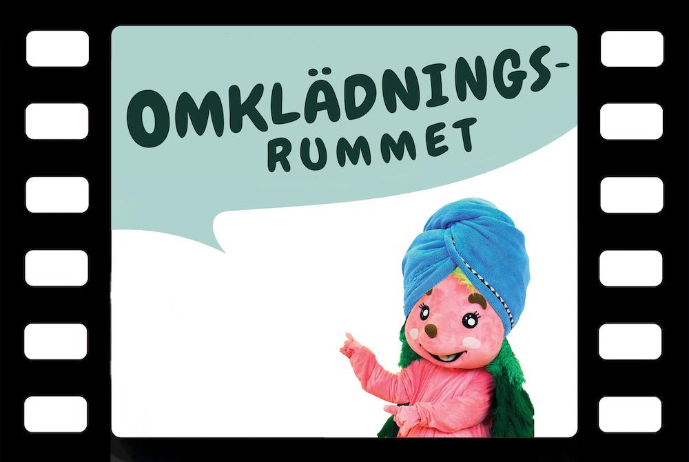 En filmruta med Triva utklädd som har en blå handduk på huvudet oh texten 'Omklädningsrummet'